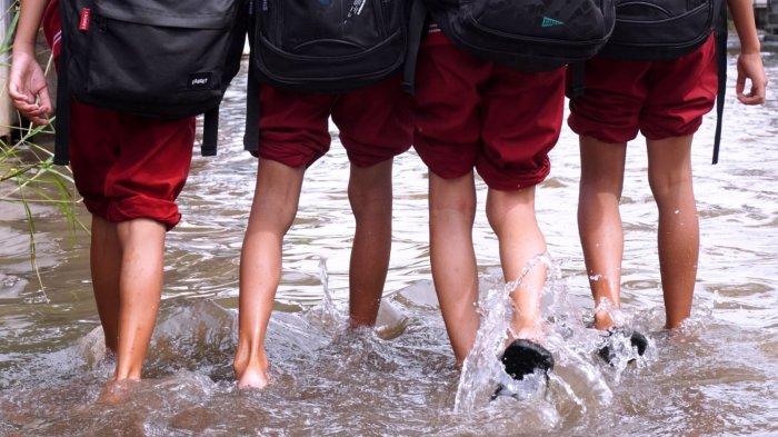 Sejumlah pelajar sekolah dasar pulang sekolah selesai mengikuti Penilaian Sumatif Akhir Semester (PSAS) Ganjil Tahun 2024 berjalan melintasi genangan banjir di Jalan Sukabirus, Desa Citeureup, Kecamatan Dayeuhkolot, Kabupaten Bandung, Jawa Barat, Senin (2/12/2024).