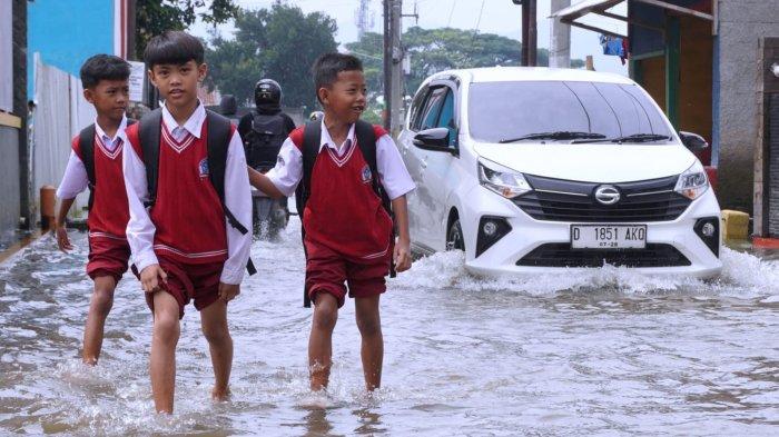 Sejumlah pelajar sekolah dasar pulang sekolah selesai mengikuti Penilaian Sumatif Akhir Semester (PSAS) Ganjil Tahun 2024 berjalan melintasi genangan banjir cileuncang di Jalan Sukabirus, Desa Citeureup, Kecamatan Dayeuhkolot, Kabupaten Bandung, Jawa Barat, Senin (2/12/2024).