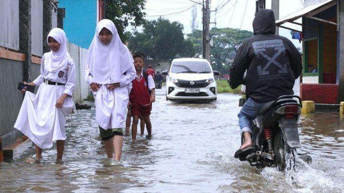 Sejumlah pelajar sekolah dasar pulang sekolah selesai mengikuti Penilaian Sumatif Akhir Semester (PSAS) Ganjil Tahun 2024 berjalan melintasi genangan banjir cileuncang di Jalan Sukabirus, Desa Citeureup, Kecamatan Dayeuhkolot, Kabupaten Bandung, Jawa Barat, Senin (2/12/2024).