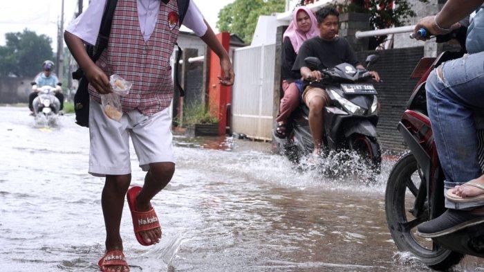 Sejumlah pelajar sekolah dasar pulang sekolah selesai mengikuti Penilaian Sumatif Akhir Semester (PSAS) Ganjil Tahun 2024 berjalan melintasi genangan banjir cileuncang di Jalan Sukabirus, Desa Citeureup, Kecamatan Dayeuhkolot, Kabupaten Bandung, Jawa Barat, Senin (2/12/2024).