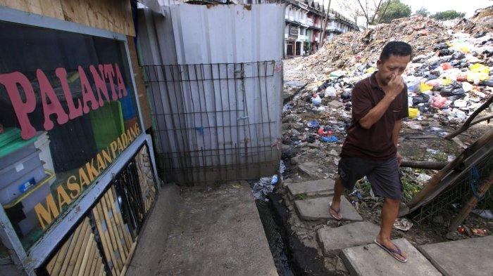Seorang warga menutup hidung saat melintasi hamparan sampah yang menggunung di area depan Pasar Induk Caringin, Jalan Soekarno Hatta, Kota Bandung, Senin (16/12/2024).