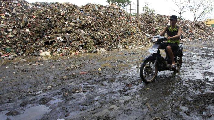 Pengendara sepeda motor melintasi jalanan yang becek di samping hamparan sampah yang menggunung di area depan Pasar Induk Caringin, Jalan Soekarno Hatta, Kota Bandung, Senin (16/12/2024).