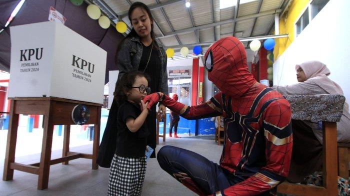 Petugas berkostum Superhero menyapa anak kecil yang ikut orang tuanya menggunakan hak pilihnya di Tempat Pemungutan Suara (TPS) 12 pada pelaksanaan Pemilihan Kepala Daerah (Pilkada) Serentak 2024, di RT 03 RW 03, Kampung Babakan Loa, Kelurahan Pasirkaliki, Kota Cimahi, Jawa Barat, Rabu (27/11/2024).