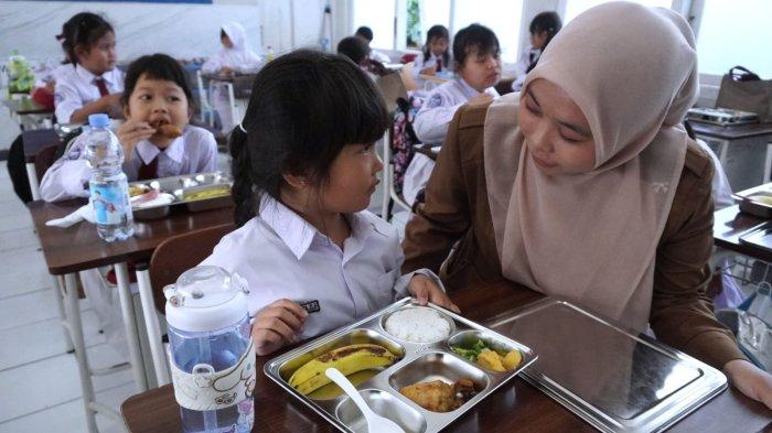 Guru mengajak seorang pelajar makanan sehat bergizi dalam program Makan Bergizi Gratis (MBG) hari pertama, di SD Angkasa, Lanud Husein Sastranegara, Kota Bandung, Jawa Barat, Senin (6/1/2025).