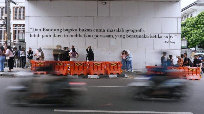 Wisatawan berfoto di bawah Jembatan Penyeberangan Orang (JPO) dengan latar belakang tulisan ungkapan Pidi Baiq 