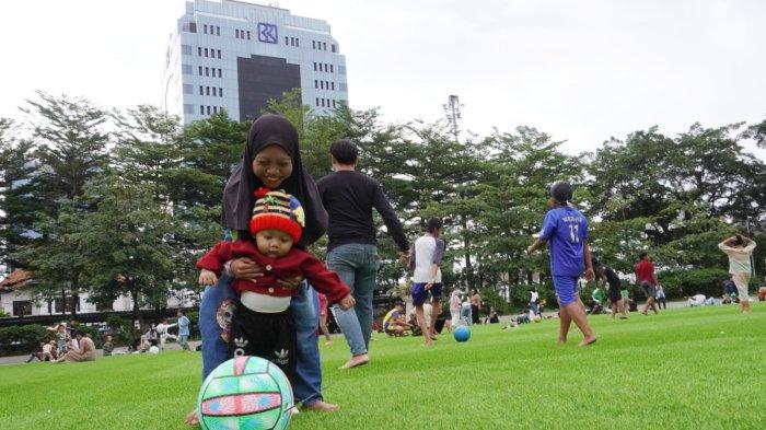 Anak kecil ditemani kakaknya bermain bola saat mengisi liburan di lapangan rumput sintetis taman Alun-Alun Kota Bandung, Jawa Barat, Selasa (28/1/2025).
