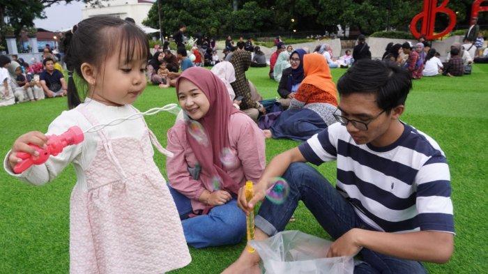 Anak kecil meniup balon sabun ditemani orang tuanya saat mengisi liburan di lapangan rumput sintetis taman Alun-Alun Kota Bandung, Jawa Barat, Selasa (28/1/2025).