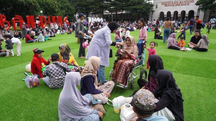 Satu keluarga bersantai sambil mengobrol saat mengisi liburan di lapangan rumput sintetis taman Alun-Alun Kota Bandung, Jawa Barat, Selasa (28/1/2025).