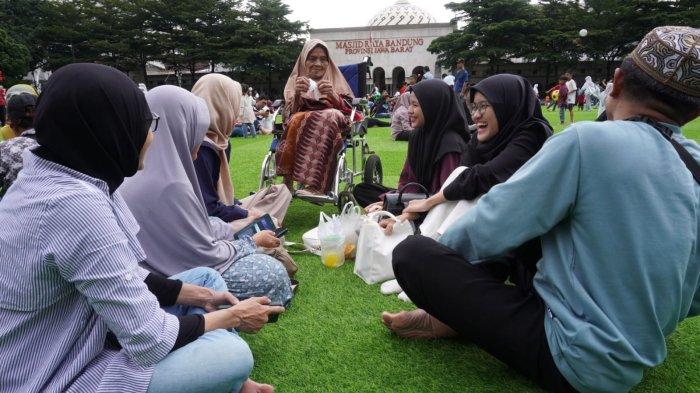 Satu keluarga bersantai sambil mengobrol saat mengisi liburan di lapangan rumput sintetis taman Alun-Alun Kota Bandung, Jawa Barat, Selasa (28/1/2025).