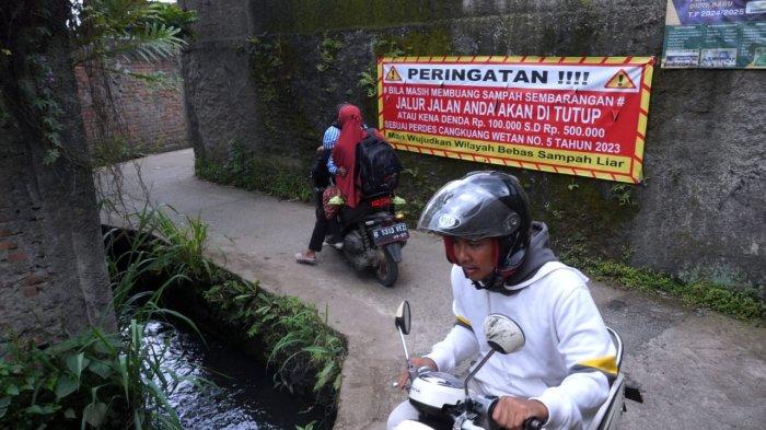 Pengendara bermotor melintasi spanduk bertuliskan himbauan untuk tidak membuang sampah sembarangan di Jalan Citra, Desa Cangkuang Wetan, Kecamatan Dayeuhkolot, Kabupaten Bandung, Jawa Barat, Selasa (18/2/2025).