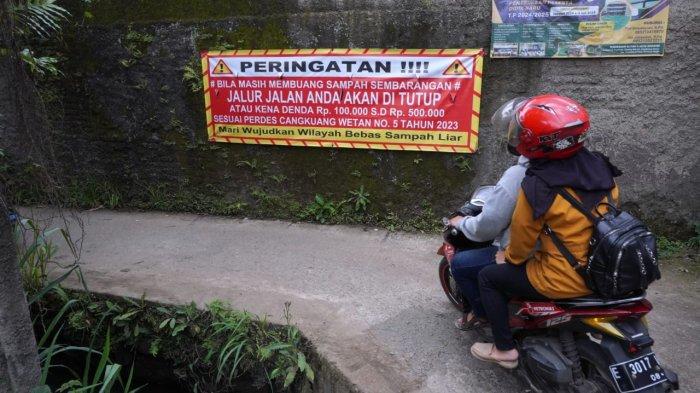 Pengendara bermotor melintasi spanduk bertuliskan himbauan untuk tidak membuang sampah sembarangan di Jalan Citra, Desa Cangkuang Wetan, Kecamatan Dayeuhkolot, Kabupaten Bandung, Jawa Barat, Selasa (18/2/2025).