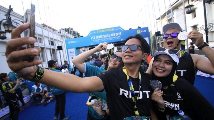 Sejumlah peserta berkalung medali berswafoto setelah masuk garis finish dalam ajang PLN Jabar Smile Run 2025, di Jalan Ir Sukarno, kawasan Gedung Merdeka, Kota Bandung, Jawa Barat, Minggu (23/2/2025).