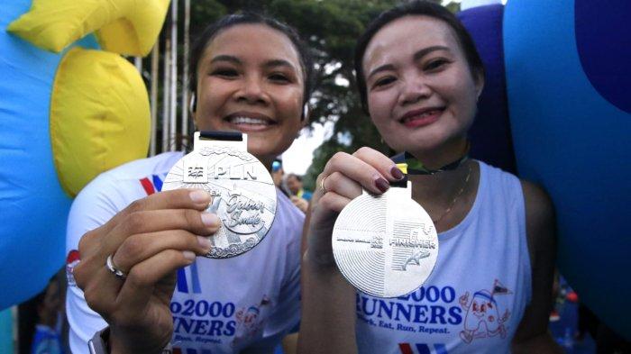 Dua orang peserta memegang medali setelah masuk garis finish dalam ajang PLN Jabar Smile Run 2025, di Jalan Ir Sukarno, kawasan Gedung Merdeka, Kota Bandung, Jawa Barat, Minggu (23/2/2025).
