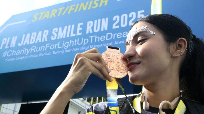 Seorang peserta memegang medali setelah masuk garis finish dalam ajang PLN Jabar Smile Run 2025, di Jalan Ir Sukarno, kawasan Gedung Merdeka, Kota Bandung, Jawa Barat, Minggu (23/2/2025).