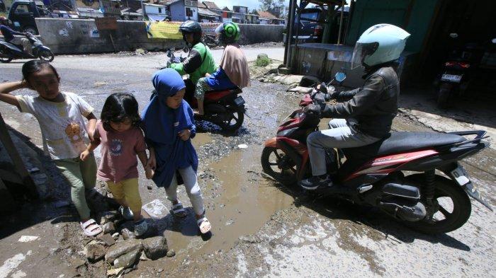 Pengguna jalan melintasi permukaan jalan rusak yang digenangi air di Jalan Ciroyom Barat, Kelurahan Ciroyom, Kecamatan Andir, Kota Bandung, Jawa Barat, Selasa (11/3/2025).