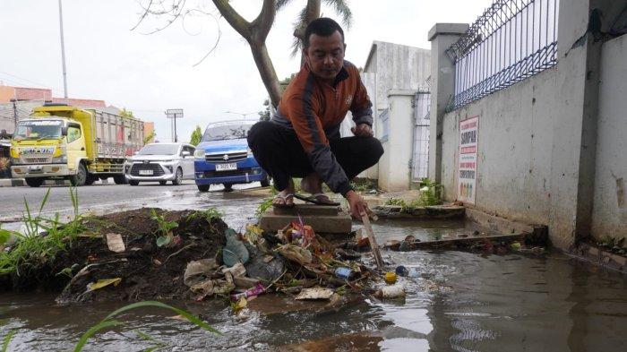 Seorang warga membersihkan sampah yang menyumbat saat air meluap dari drainase atau selokan di Jalan Raya Gading Tutuka, Desa Cincin, Kecamatan Soreang, Kabupaten Bandung, Jawa Barat, Jumat (11/4/2025).
