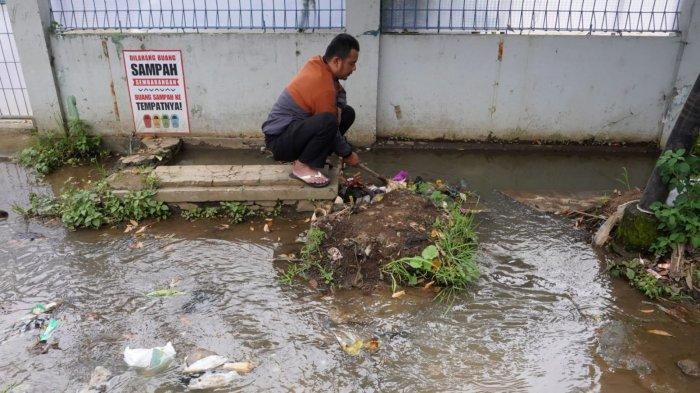 Seorang warga membersihkan sampah yang menyumbat saat air meluap dari drainase atau selokan di Jalan Raya Gading Tutuka, Desa Cincin, Kecamatan Soreang, Kabupaten Bandung, Jawa Barat, Jumat (11/4/2025).