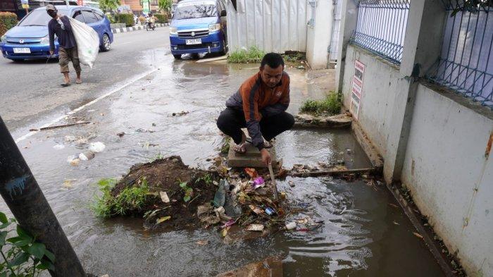 Seorang warga membersihkan sampah yang menyumbat saat air meluap dari drainase atau selokan di Jalan Raya Gading Tutuka, Desa Cincin, Kecamatan Soreang, Kabupaten Bandung, Jawa Barat, Jumat (11/4/2025).