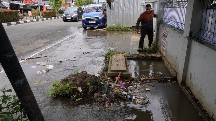 Seorang warga melintas di samping genangan air di bahu jalan yang meluap dari drainase atau selokan di Jalan Raya Gading Tutuka, Desa Cincin, Kecamatan Soreang, Kabupaten Bandung, Jawa Barat, Jumat (11/4/2025).