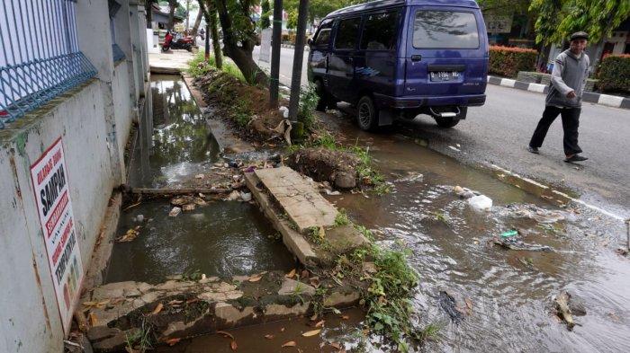 Seorang warga melintas di samping genangan air di bahu jalan yang meluap dari drainase atau selokan di Jalan Raya Gading Tutuka, Desa Cincin, Kecamatan Soreang, Kabupaten Bandung, Jawa Barat, Jumat (11/4/2025).