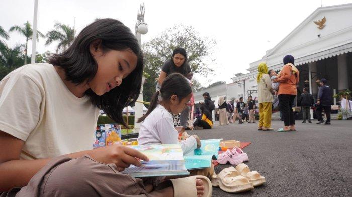 Dua orang anak membaca buku yang disediakan Mobil Perpustakaan Keliling dalam gelaran Abdi Nagri Nganjang Ka Warga edisi pertama, di halaman Gedung Pakuan, Jalan Otto Iskandardinata, Kota Bandung, Jawa Barat, Sabtu (12/4/2025).