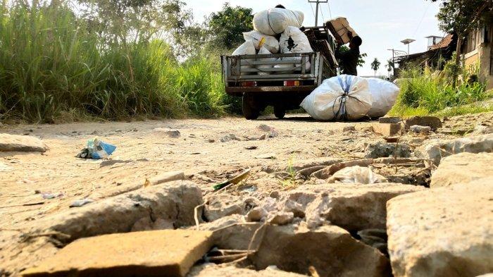 Warga memasukan barang ke mobil di Jalan Inspeksi Citarum dengan permukaan rusak, di Desa Mekarrahayu, Kecamatan Margaasih, Kabupaten Bandung, Jawa Barat, Selasa (6/5/2025).