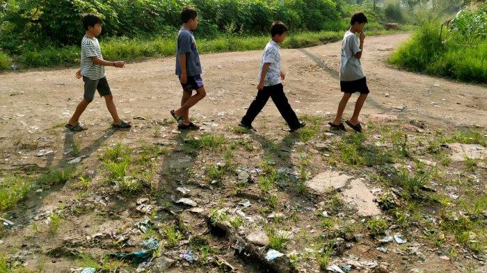 Sejumlah anak melintas di Jalan Inspeksi Citarum dengan permukaan rusak, di Desa Mekarrahayu, Kecamatan Margaasih, Kabupaten Bandung, Jawa Barat, Selasa (6/5/2025).