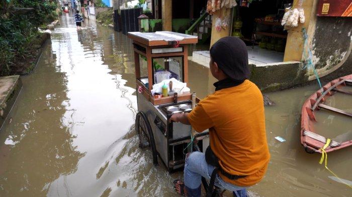 Warga melintasi banjir yang merendam jalan di Kampung Bojongasih, Desa/Kecamatan Dayeuhkolot, Kabupaten Bandung, Jawa Barat, Kamis (15/5/2025).