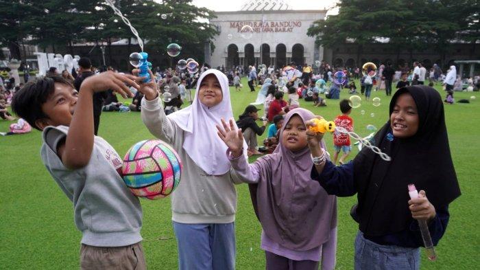 Warga mengisi liburan di lapangan rumput sintetis Taman Alun-alun Kota Bandung, Jawa Barat, Jumat (27/6/2025).