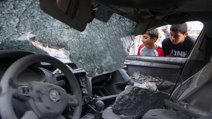 Dua warga Palestina memeriksa kabin mobil yang rusak akibat gempuran militer Israel di Gaza City, Selasa (10/10/2923).