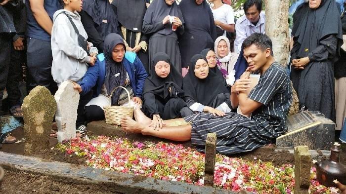 DUKA MENDALAM: Rachmat Irianto (Rian), duduk di samping pusara ayahnya Bejo Sugiantoro di TPU Geluran memeluk erat foto mendiang ayahnya setelah selesai proses penguburan di TPU Geluran, Sidoarjo. Rabu (26/2/2025).