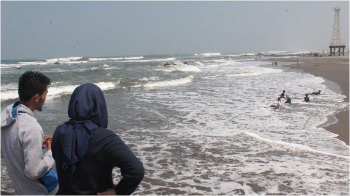 Pengunjung berswafoto di tumpukan beton pemecah ombak di Pantai Jayanti sambil memandang ke arah menara pengawas