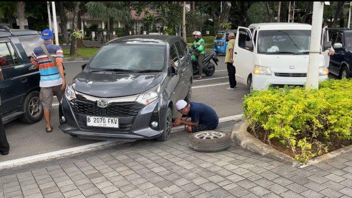 Hasan, wisatawan asal Senen, Jakarta Pusat tampak sibuk mengganti ban mobilnya yang kempis saat parkir di sekitar kawasan Monas, Gambir, Rabu (2/4/2025).