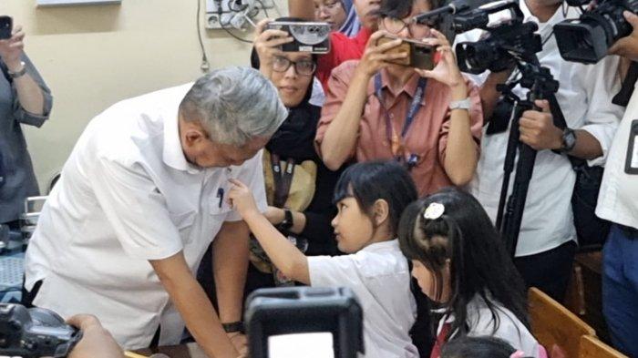 Momen siswi SD penasaran dengan lencana wamen yang ada di dada kiri Wakil Menteri Sosial, Agus Jabo Priyono, yang meninjau pelaksanaan hari pertama makan bergizi gratis di salah satu sekolah swasta di Jakarta Barat, Senin (6/1/2025).
