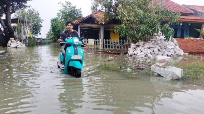 TEROBOS ROB - Seorang pengendara motor terobos genangan air rob di Kecamatan Sayung, Kabupaten Demak, Jumat (20/6/2025). Imbas dari banjir rob tersebut, tak sedikit pengendara motor mengeluhkan kendaraannya mudah rusak.