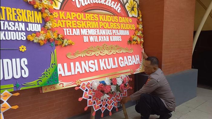 KARANGAN BUNGA - Anggota Polres Kudus tengah merapikan karangan bunga yang terpajang di halaman kantor Polres Kudus, Senin (21/7/2025). Total ada 10 karangan bunga yang berisi dukungan atas penindakan kasus judi oleh Polres Kudus. (Foto: Tribunnjateng/Rifqi Gozali).