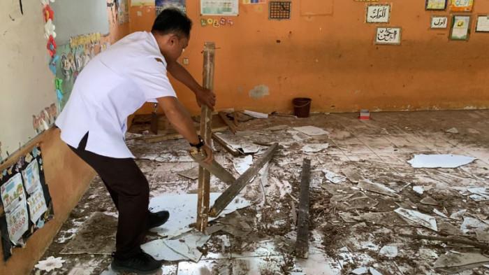 TATA KAYU KEROPOS - Seorang guru di SDN Kawengen 02, Kawengen, Ungaran Timur, Kabupaten Semarang menata reruntuhan atap kayu yang runtuh, keropos dan berserakan di lantai ruang kelas 2, Rabu (30/7/2025). Ruang kelas itu tidak bisa dipakai sehingga pihak sekolah menerapkan jam belajar siang.