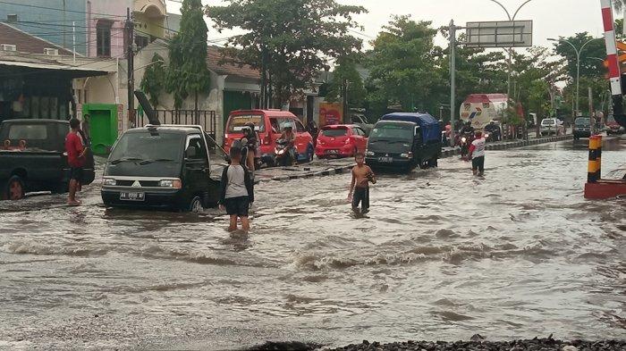 Anak-anak membantu warga menyeberangi genangan banjir di jalan Muktiharjo Lor Semarang dekat perlintasan rel kereta api, Selasa (28/11/2023).