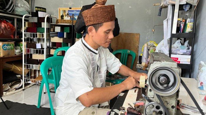 JAHIT PECI - Faizin, produsen Peci Sobo di kiosnya Desa Sojokerto Kecamatan Leksono Wonosobo sedang menjahit bahan menjadi peci yang tahan air dan bisa dicuci, Kamis (21/3/2025)