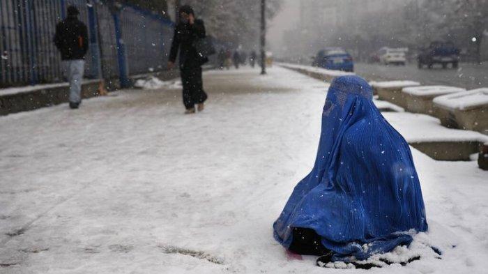 Seorang wanita Afghanistan mengenakan burka, kanan, memohon di atas salju di Kabul, Afghanistan, Minggu, 6 Februari 2022. (AP PHOTO/HUSSEIN MALLA)