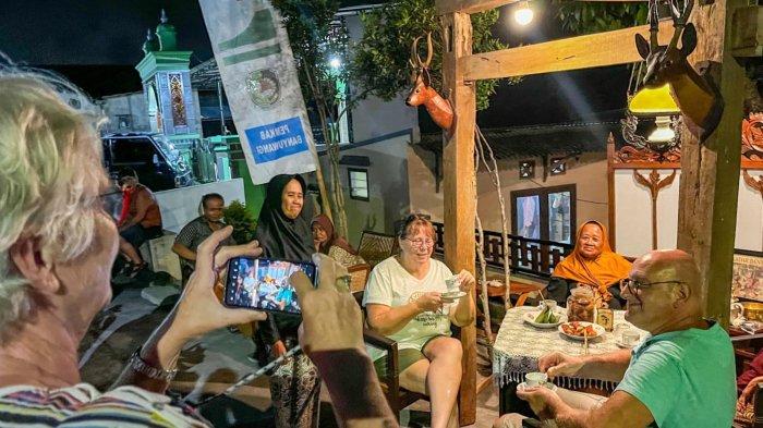 Wisatawan asing menikmati kopi di teras rumah warga dalam Festival Ngopi Sepuluh Ewu yang digelar di sepanjang jalan utama Desa Kemiren pada Rabu malam (6/11/2024). 