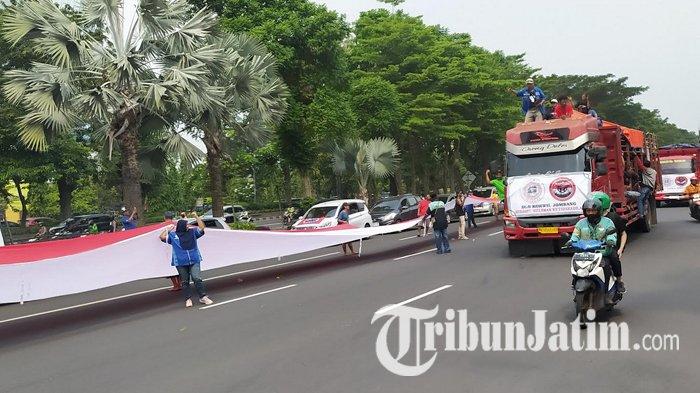 BENDERA - Massa aksi yang mengatasnamakan Gerakan Sopir Jawa Timur (GSJT) mulai berdatangan di Jalan Frontage Ahmad Yani, Surabaya, Kamis (19/6/2025) sekitar pukul 12.00 WIB. Seraya membawa bendera panjang, massa menggelar long march untuk berorasi di depan Gedung Dishub Jatim, lalu berlanjut ke Mapolda Jatim. 