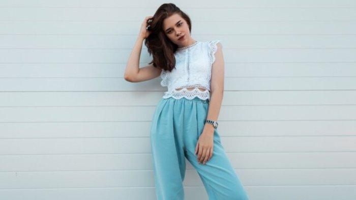 Elegant pretty young woman straightens hair. Cute girl in a trendy lace blouse in vintage blue pants posing
