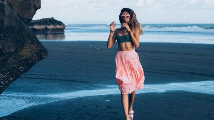 Caucasian fit tanned woman in tiny top and pink skirt on black sand beach