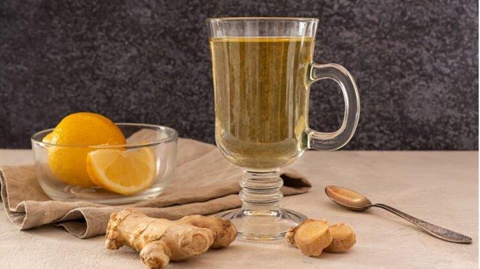 A glass of hot ginger and lemon tea with slices of lemon and ginger root on wooden table