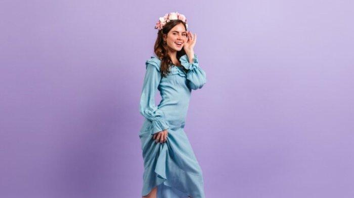 Lovely smiling lady in satin blue outfit. Woman touches her face on lilac wall