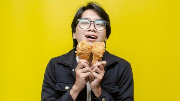 Expressive asian man eats and smells fried chicken drumstick with face full of satisfication