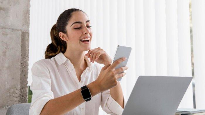 PANTUN SEMANGAT KERJA - Potret wanita tertawa melihat smartphone saat bekerja dari Freepik.com, Selasa (20/5/2025). Lihat kumpulan pantun semangat kerja buat pacar berikut ini, dijamin bikin mood membaik, yuk kirimkan.