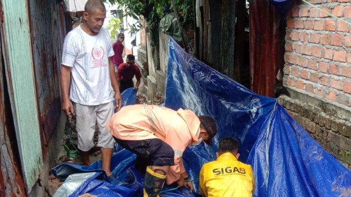 Warga dan petugas menutupi jalan terdampak pergerakan tanah di Jalan Telaga Sari, Balikpapan, Selasa (26/12/2023). Beruntung, tidak ada korban jiwa, dan BPBD Balikpapan berkoordinasi untuk pemasangan terpal dan pengecekan kondisi tanah. Warga diimbau waspada terhadap risiko longsor, dan penanganan melibatkan BPBD, TRC PB, SAR Brimob, dan masyarakat setempat.