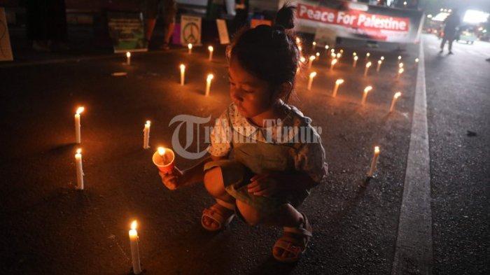 Anak dari peserta aksi yang tergabung dalam Aliansi Perdamaian ikut Aksi bakar 1000 lilin yang berlangsung di depan Monumen mandala, Jl Jend Sudirman, Makassar, Kamis (19/10/2023) malam. Aksi bakar lilin sebagai simbolisasi kepedulian atas penderitaan rakyat Palestina atas kekejaman Negara Israel.